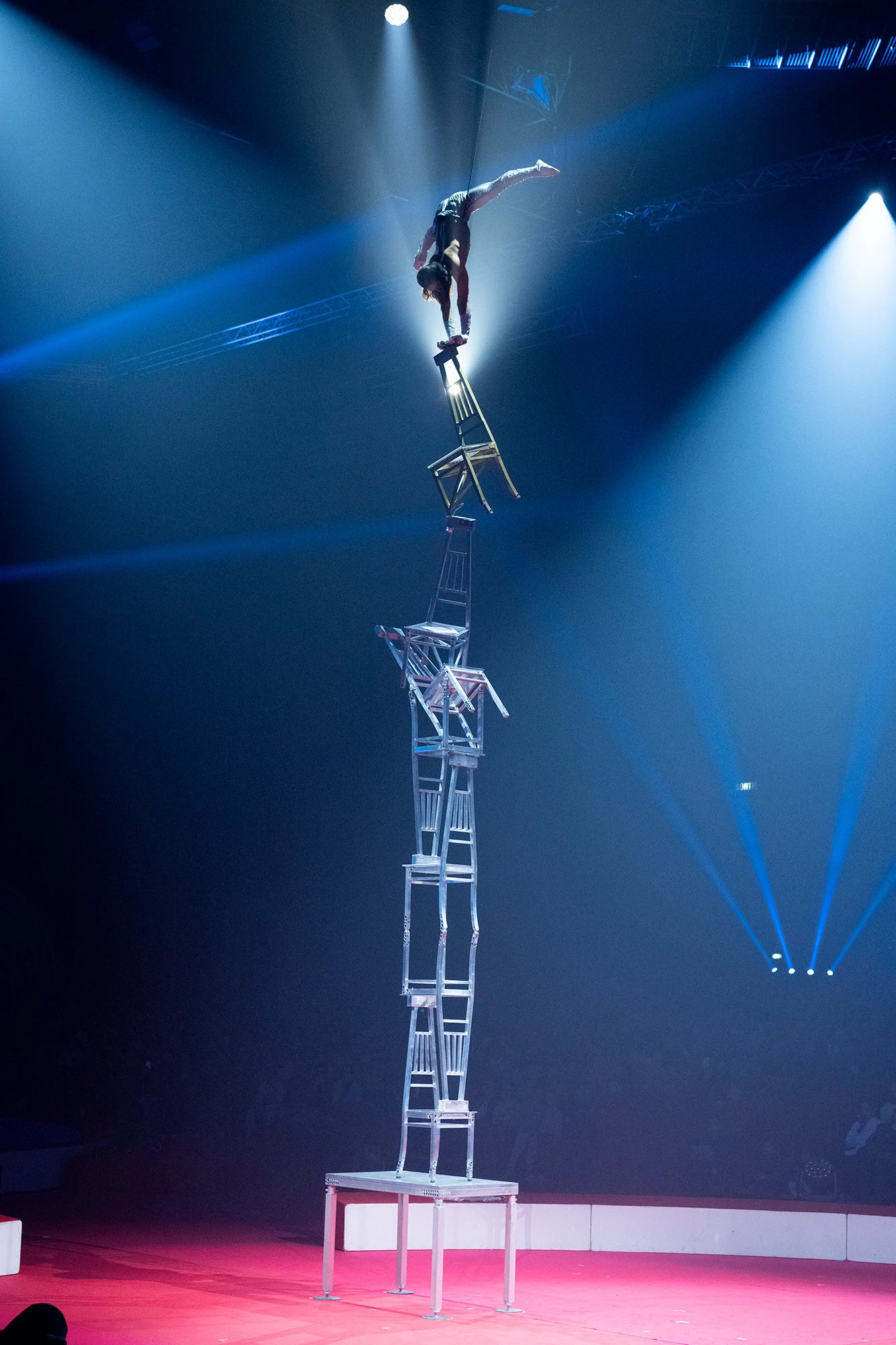 Ochir holding a balance at the top of a tall stack of chairs under a spotlight