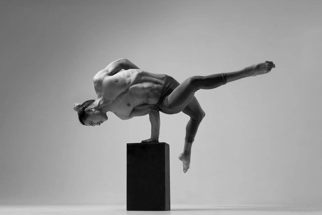 Ochir holding a one-arm hand balance on a block in the studio